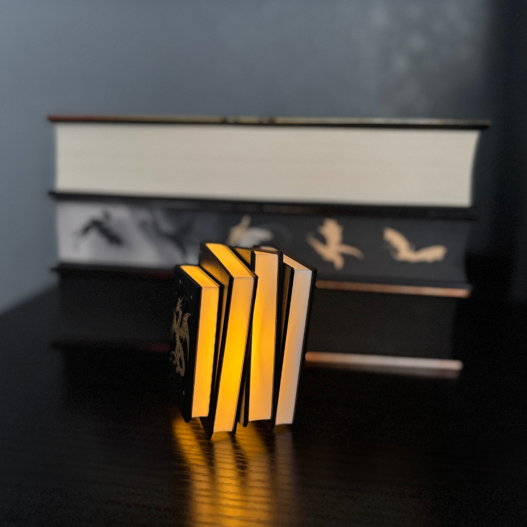 View of the Fantasy Dragon Book Light glowing and standing up in front of a stack of fantasy books.