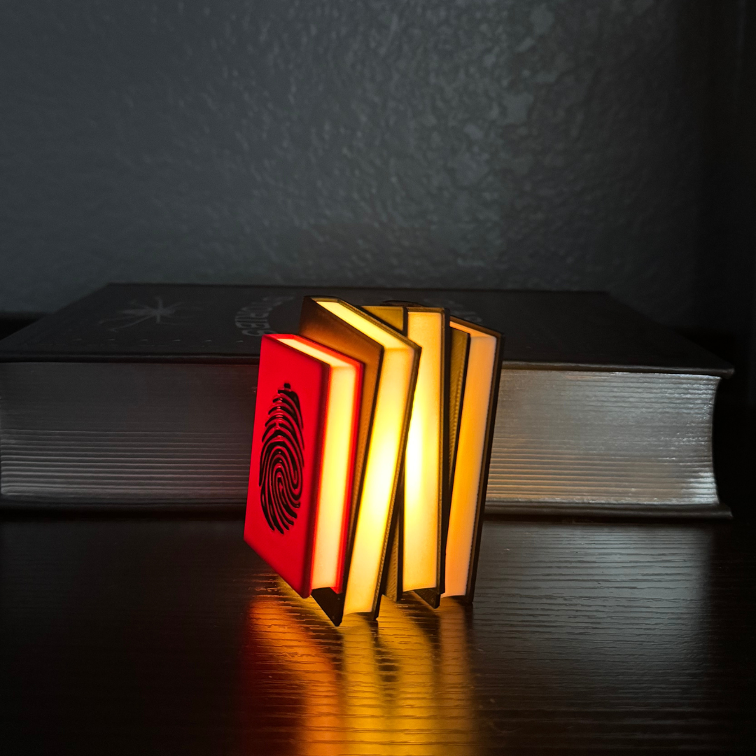 View of the True Crime Book Light glowing and standing up in front of a stack of true crime books.