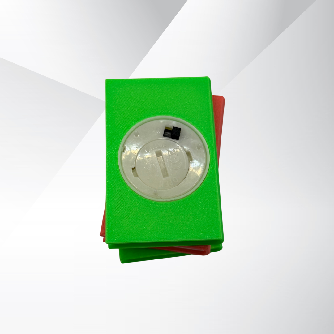 The bottom view of the neon green and pink light up stack of books, showing the on and off switch and where the batteries can be replaced on a white and silver background.