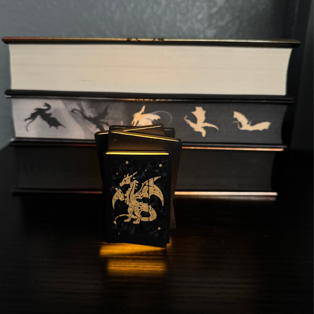 View of the front cover of the Fantasy Dragon Book Light glowing and standing up in front of a stack of fantasy books.