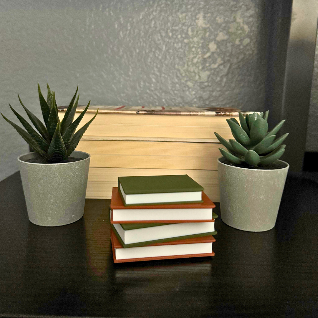 Cozy brown and green light up book stack sitting on a bookshelf surrounded by plants and books.