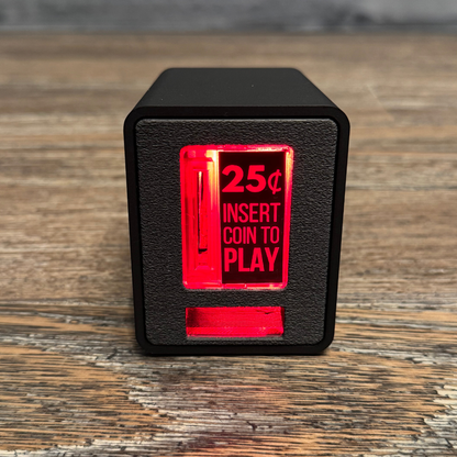 Studio close-up of the black TinyBrights™ Insert Coin Cube showing the arcade-style coin slot and front panel on wooden table.