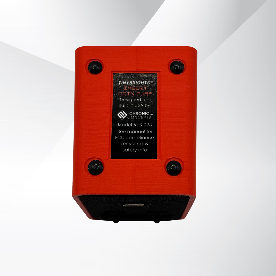 Bottom view of the TinyBrights™ Insert Coin Cube in red, showing the product label with model information, FCC notice, and design details from Chronic Concepts.
