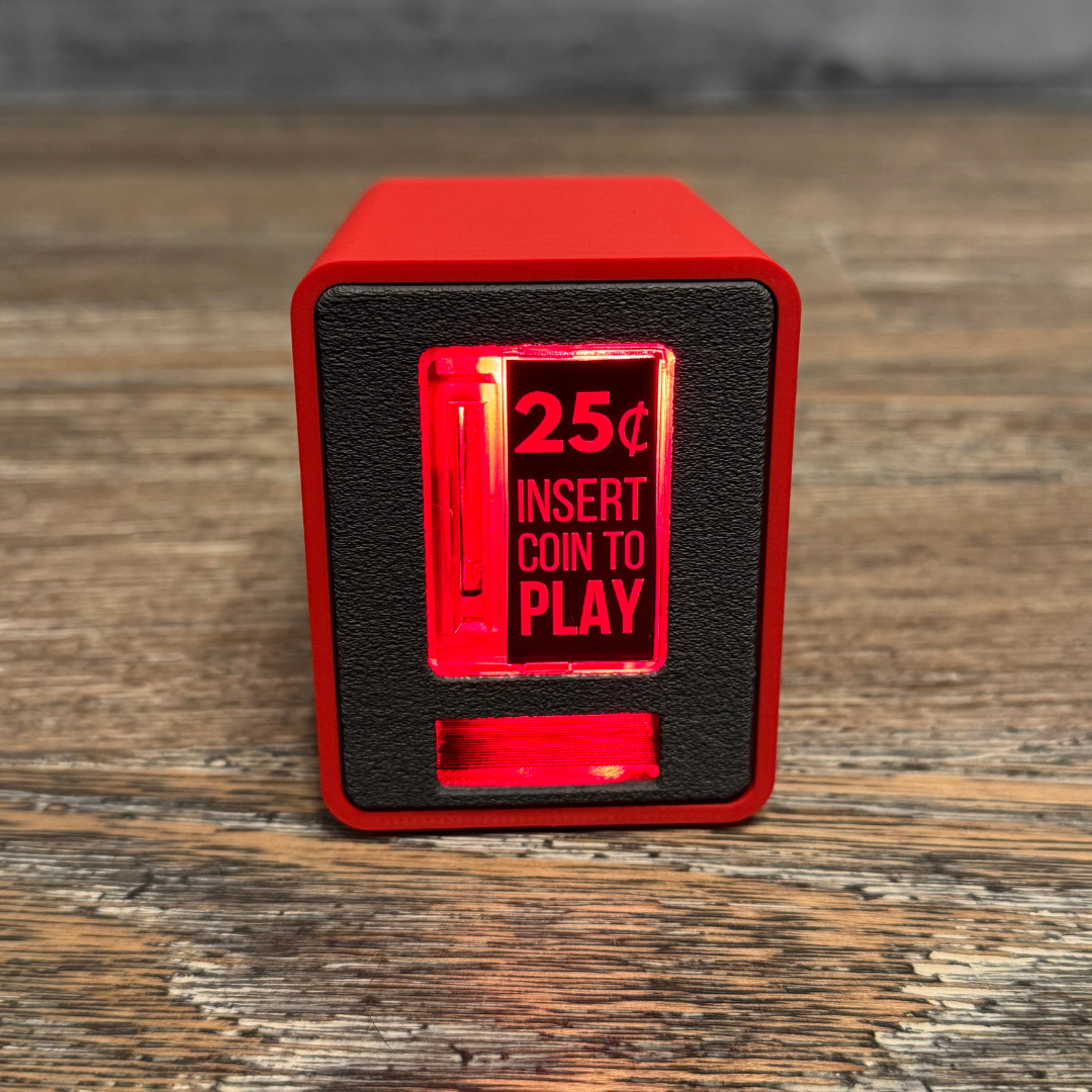 Studio close-up of the red TinyBrights™ Insert Coin Cube showing the arcade-style coin slot and front panel on wooden table.