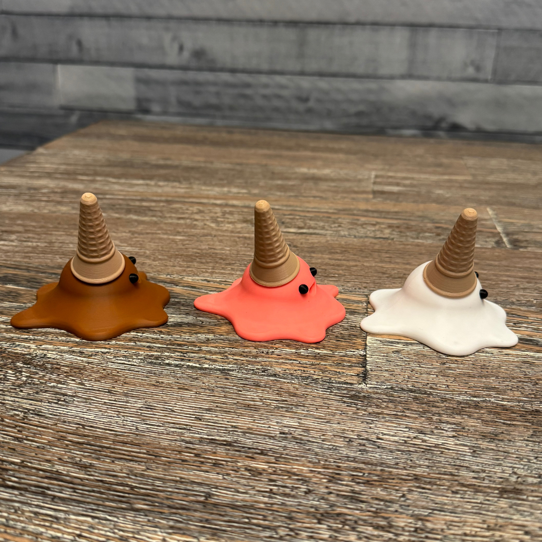 Left side view of three 3d printed melting ice cream cones made by Chronic Concepts sitting on a wooden table. Chocolate, Strawberry, and Vanilla flavored.