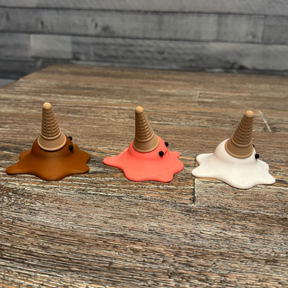 Left side view of three 3d printed melting ice cream cones made by Chronic Concepts sitting on a wooden table. Chocolate, Strawberry, and Vanilla flavored.
