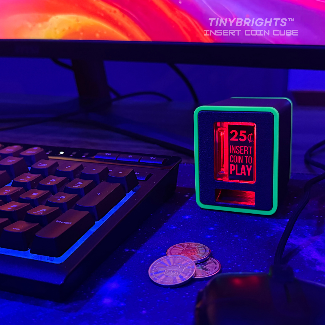 TinyBrights™ Insert Coin Cube with neon green trim glowing beside a gaming keyboard and coins, set in a purple and blue RGB-lit workstation.