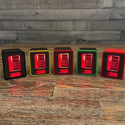 Lineup of five TinyBrights™ Insert Coin Cubes lit with red LEDs, showing color trim options in yellow, red, green, and black on a wood tabletop.