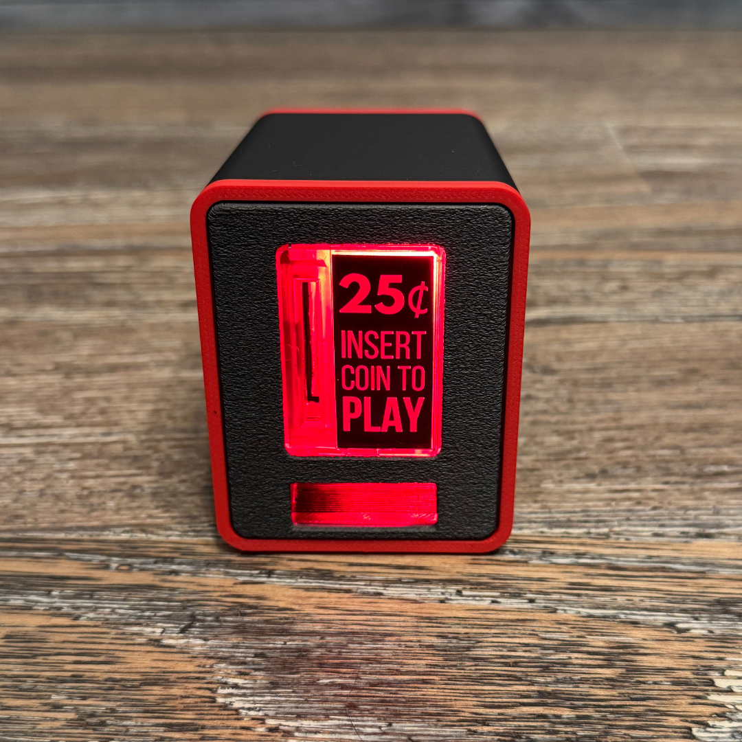 Studio close-up of the red TinyBrights™ Insert Coin Cube showing the arcade-style coin slot and front panel on wooden table.