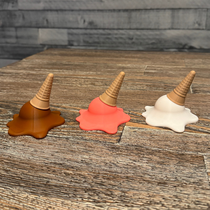 Right side view of three 3d printed melting ice cream cones made by Chronic Concepts sitting on a wooden table. Chocolate, Strawberry, and Vanilla flavored.
