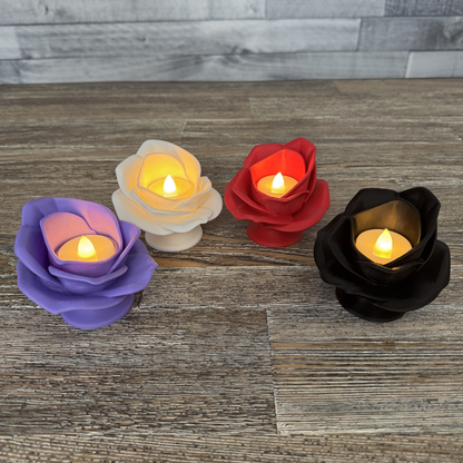 Four 3d printed rose tea light holders with their tea lights turned on sitting on a wooden table. Lilac, magenta, red, and black roses are shown.