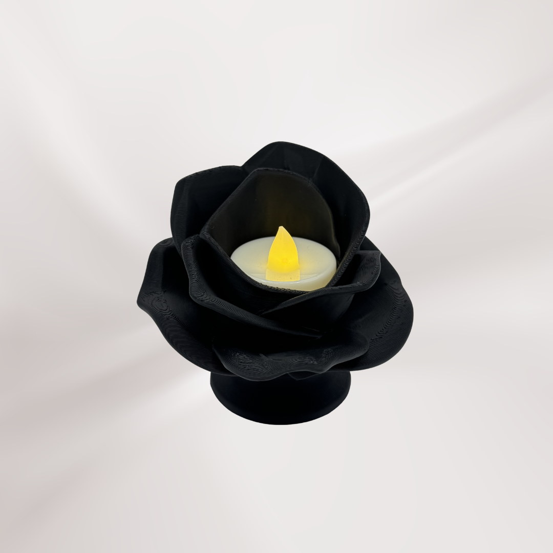A black 3d printed rose tea light holder with a tea light turned on, on an off white background.