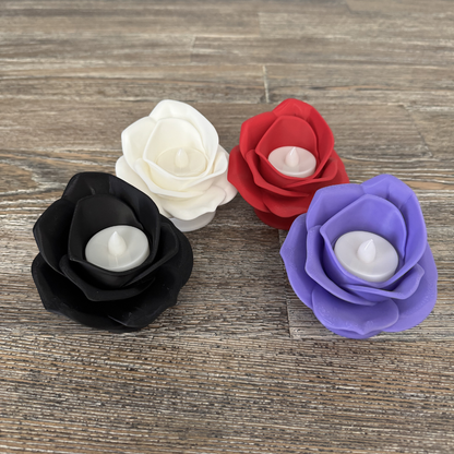 Four 3d printed rose tea light holders with their tea lights turned off sitting on a wooden table. Black, white, magenta, and lilac roses.