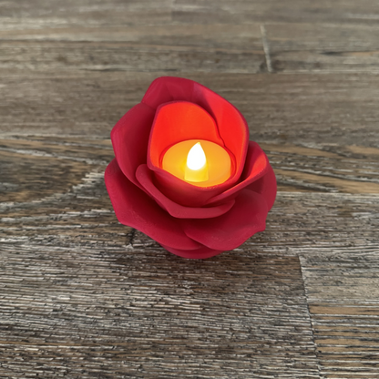 3d printed red rose tea light holder with a tea light turned on sitting on a wooden table.
