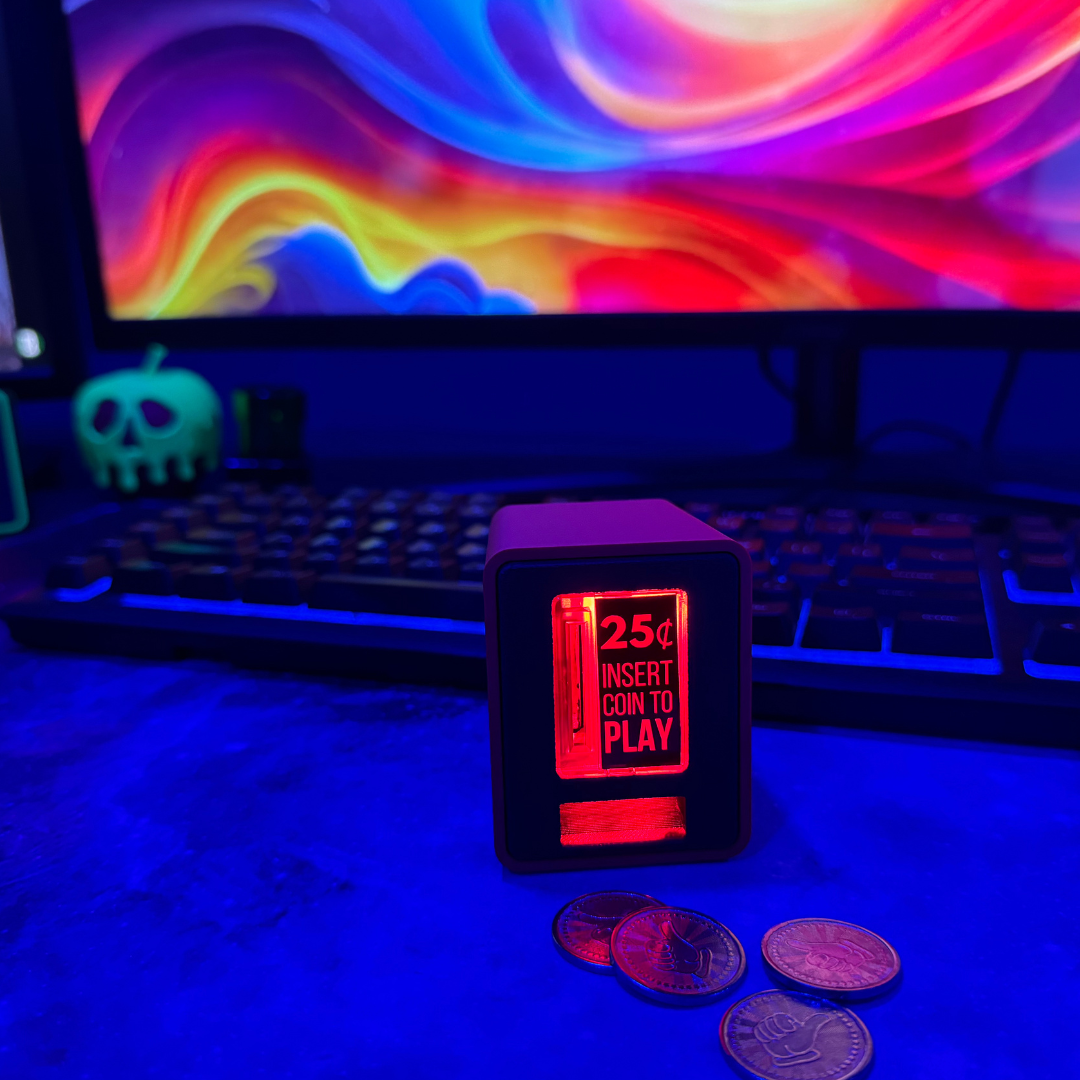 Single TinyBrights™ Insert Coin Cube illuminated on a blue-lit gaming desk with coins displayed in front and a vibrant, multicolor PC screen behind it.