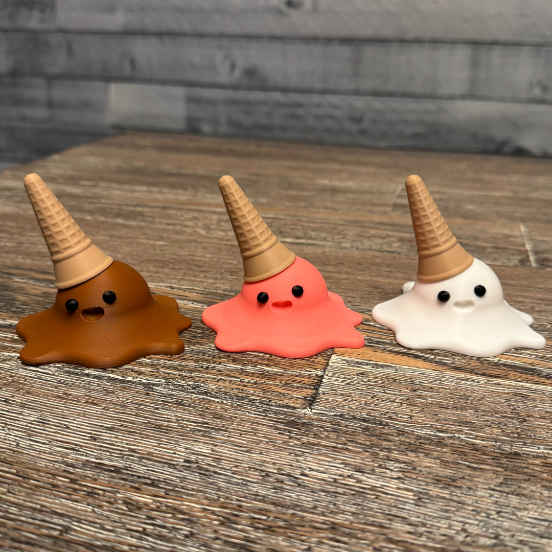 Three 3d printed melting ice cream cones made by Chronic Concepts sitting on a wooden table. Chocolate, Strawberry, and Vanilla flavored.