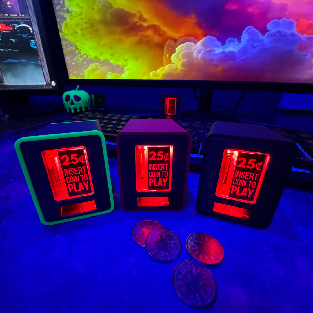 Three TinyBrights™ Insert Coin Cubes glowing in red on a gaming desk setup, surrounded by collectible tokens with a colorful PC monitor in the background.