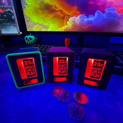 Three TinyBrights™ Insert Coin Cubes glowing in red on a gaming desk setup, surrounded by collectible tokens with a colorful PC monitor in the background.