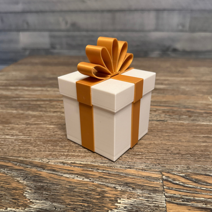 White Christmas package light with a gold bow sitting on a wooden table.