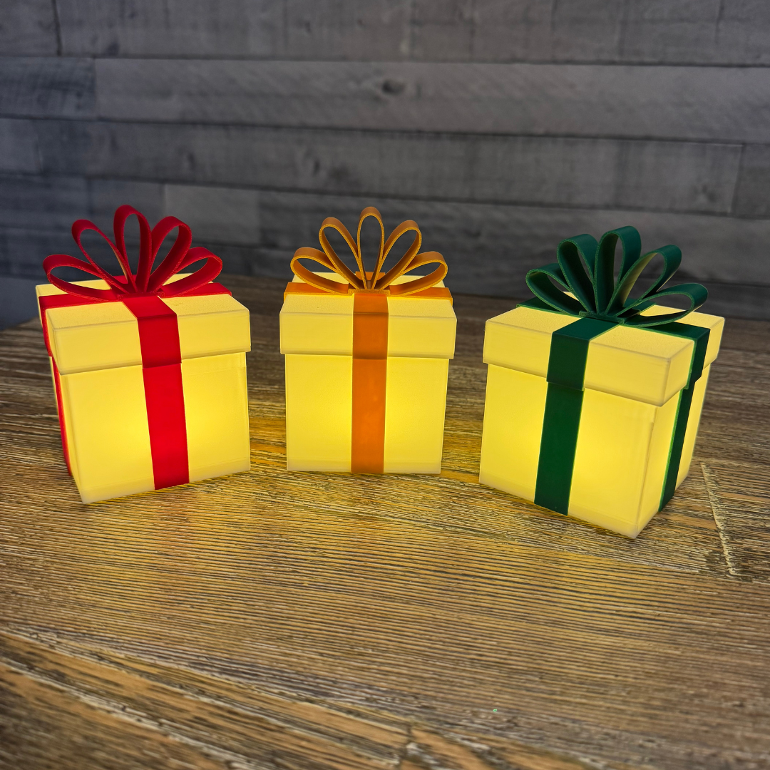 Three Christmas packages lit up sitting on a wooden table.