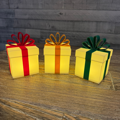 Three Christmas packages lit up sitting on a wooden table.