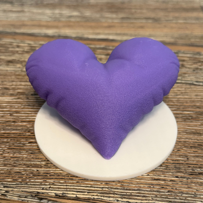 A purple 3d printed heart sculpture with a white base sitting on a wooden table.